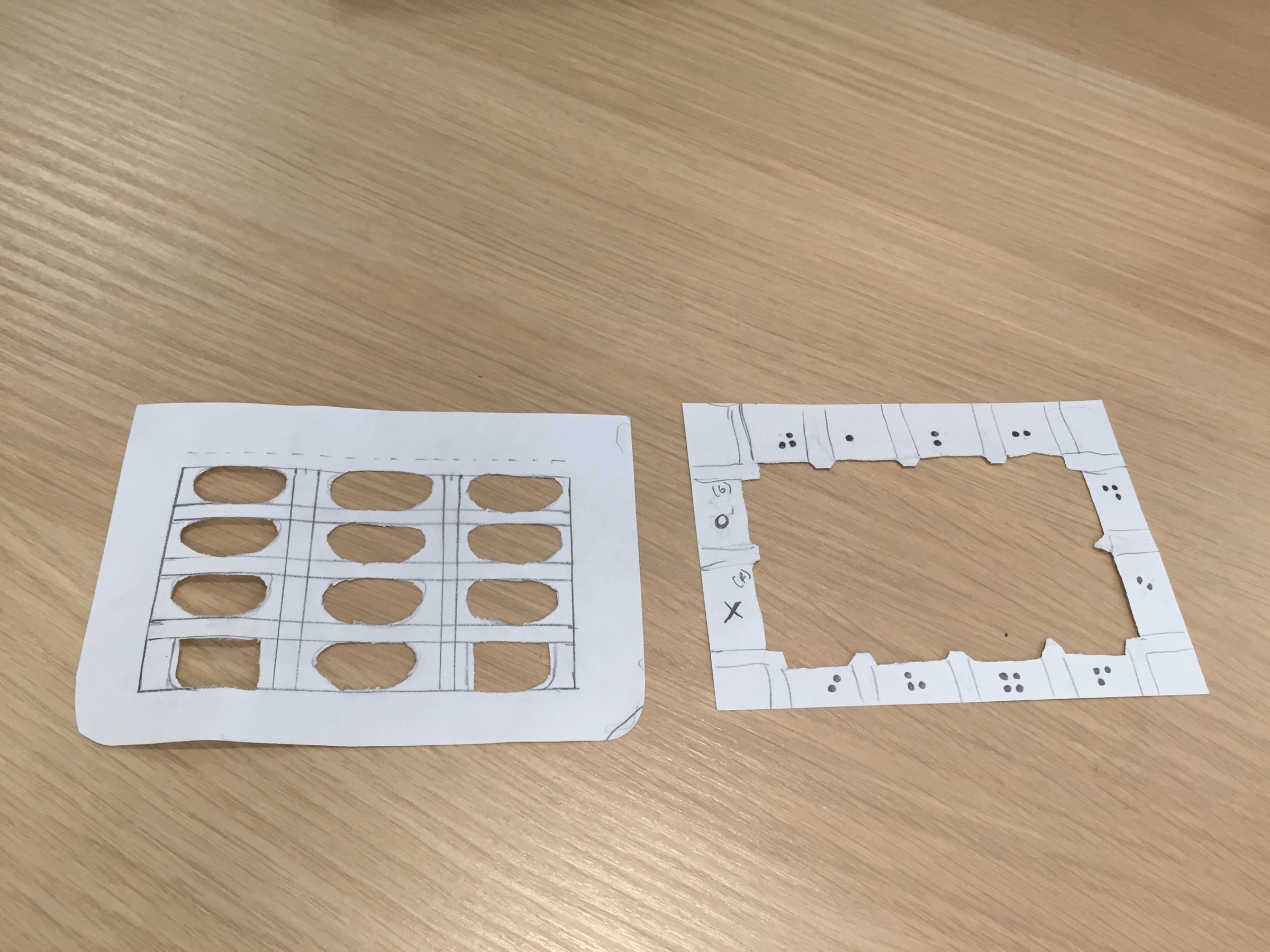 Two paper templates cut by hand, one a keypad grid and one a frame with Braille dots