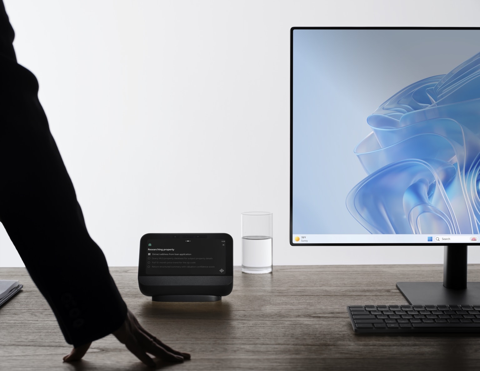 The desk companion on a desk beside a monitor running Windows, reaching for it mid-task — the device as a PC companion rather than a replacement